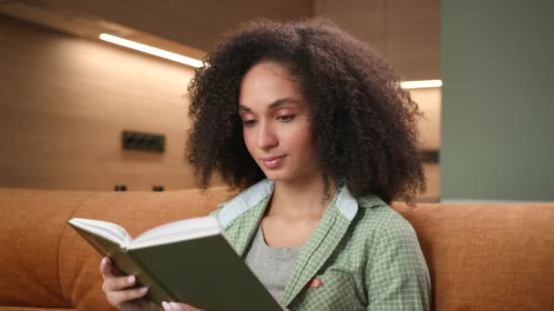 自宅で本を読んでいる女性 アフリカ系アメリカ人女性は 単独でソファーに座っている文学を読むのが好きです 4Kについて — ストック動画