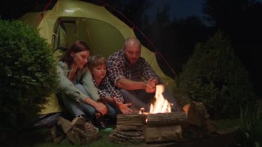 Geceleri kamp ateşinin yanında çadırda oturan çocuklu bir aile. İyi akşamlar kamp ateşi konuşması. Anne, baba ve Kid birlikte kamp yapıyorlar. 4K