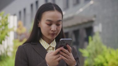 Dışarıda cep telefonu kullanan Asyalı iş kadını. Odaklanmış kadın akıllı telefonu, kapat. 4K