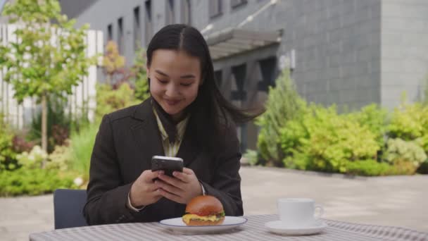 Azjatka Przegląda Telefon Komórkowy Hamburgery Zewnątrz Bizneswoman Lunch Kawiarni Czyta — Wideo stockowe