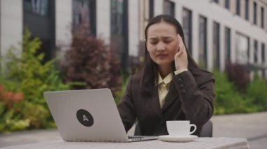 Asyalı iş kadını dizüstü bilgisayarla baş ağrısı çekiyor. Dışarıda oturan migrenden muzdarip bir kadın. 4K