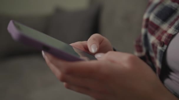 女人在沙发上浏览手机 金发20多岁的女性坐在家里用智能手机发短信聊天 — 图库视频影像