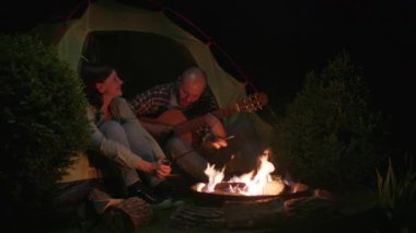 Gece Kampı 'nın Çadırında Oturan Gitar Çalan Adam. Çiftler birlikte romantik bir hafta sonu geçiriyorlar. 4K