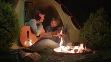 Annem gitar çalıyor ve Kid 'le şarkı söylüyor geceleri kamp ateşinin yanında çadırda oturuyor. Mutlu aile karanlıkta ateşin başında şarkı söylüyor. 4K