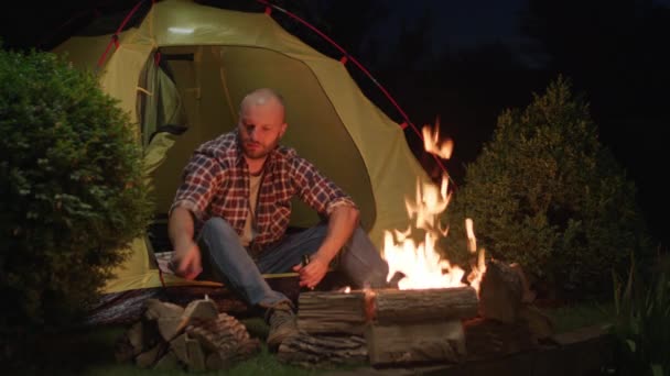 一个人坐在篝火边的帐篷里喝啤酒 一个孤独的旅行者晚上烤香肠喝啤酒4K — 图库视频影像