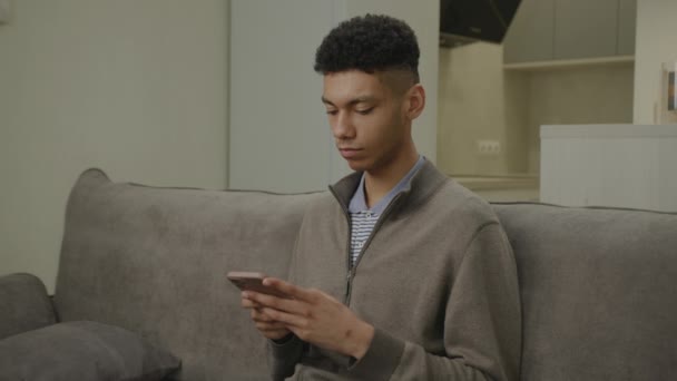 黑人在沙发上浏览手机 非裔美国人坐在家里用智能手机上网 — 图库视频影像