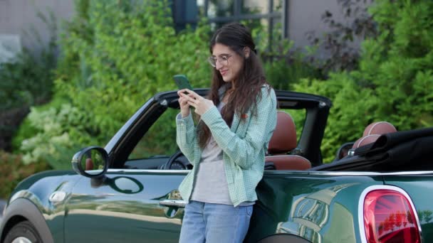 白人妇女使用手机站在外面的汽车附近 女人们对着相机微笑 在智能手机上浏览 — 图库视频影像