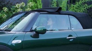 Cabrio 'nun çatısını açan kadın kameraya gülümsüyor. Üstü açık arabada oturan genç bir kadın. 4K