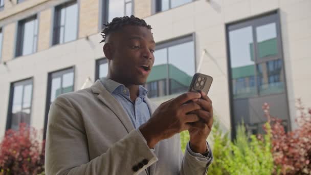ブラックビジネスマンは携帯電話で良いニュースを受け取ります 外でスマートフォンを使用してアフリカ系アメリカ人の起業家 4Kについて — ストック動画