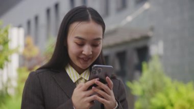 Dışarıda cep telefonunda yazan kadın. 20 'li yaşlarda Asyalı bir kadın sokakta akıllı telefonuyla internette sörf yapıyor. 4K