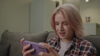 Akıllı telefon kullanan bir kadın video oyunu oynuyor. 20 'li yaşlarda bir kadın evdeki koltukta oturmuş cep telefonu oyunu oynuyor. 4K