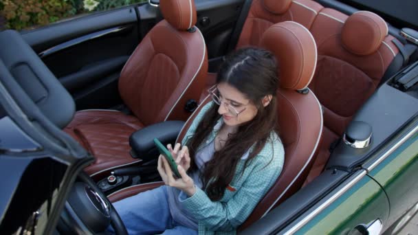 女人坐在敞篷车里用手机发短信 女司机在浏览她的智能手机 — 图库视频影像