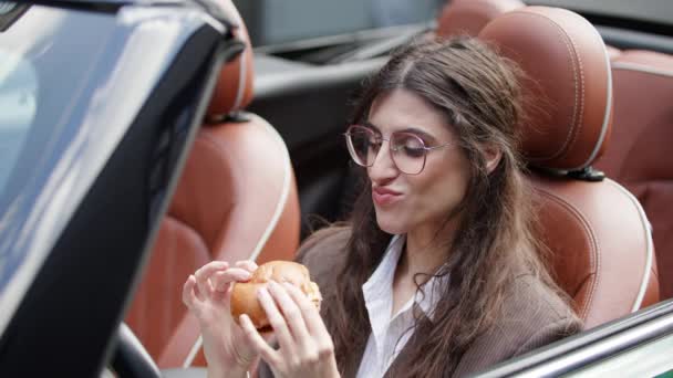 コンバーチブルカーでバーガーを食べる女性 ハンガリーの女性ドライバーが車でファストフードを食べる 4Kについて — ストック動画