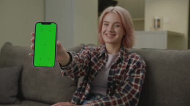 Kamera 'da Yeşil Ekran Akıllı Telefonu Tutan Kadın. Gülümseyen 20 'li yaşlarda bir kadın kameraya krom ekranlı cep telefonu gösteriyor. 4K