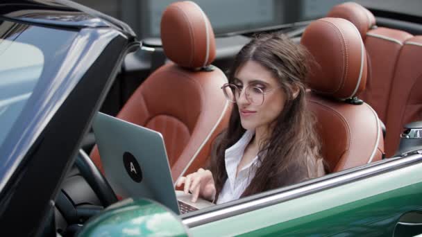 女商人坐在车顶上使用笔记本电脑 年轻的成年妇女在网上从事可转换工作 — 图库视频影像