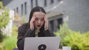 Bilgisayarında kötü haber okuyan Asyalı kadın. Dışarıda dizüstü bilgisayar kullanan üzgün bir iş kadını. 4K