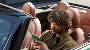 Üstü açık arabada oturan adam cep telefonuna bakıyor. 20 'li yaşlarda Hintli erkek sürücü telefon kullanarak daktilo yazıyor. 4K