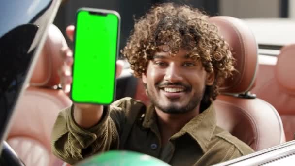カメラで電話グリーン画面を表示するドライバー 車に座っているクロマキーのスマートフォン画面を保持しているインド人男性 4Kについて — ストック動画