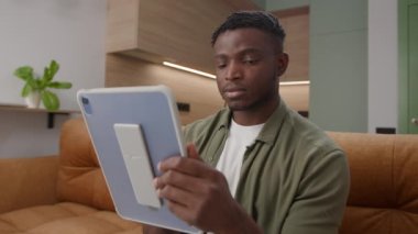 Koltukta Siyah Adam Tablet Bilgisayarı 'na bakıyor. Dijital tablet kullanan Afrikalı Amerikalı bir erkek. 4K