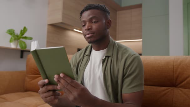 Μαύρος Άντρας Που Διαβάζει Βιβλίο Καθισμένος Στον Καναπέ Στο Σπίτι — Αρχείο Βίντεο