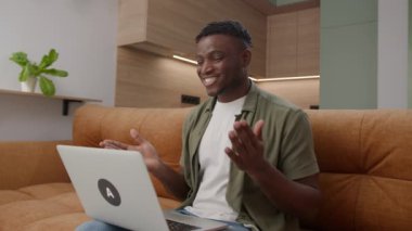 Video 'daki Siyah Adam Laptop kullanıyor. Afrikalı Amerikalı adam evde çalışan bilgisayarla konuşuyor. 4K