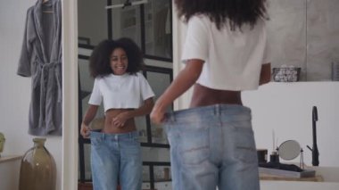 Kilo verdikten sonra Big Jeans giyen bir kadın. Siyah kadın kilo verdikten sonra yansımasına hayran. 4K