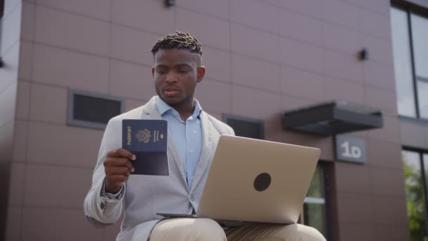 ブラックマン パスポートを保持し ラップトップで入力します 30代のビジネスマンが外で働いています 4Kについて — ストック動画