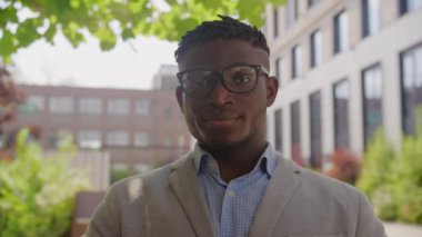 Siyah iş adamı, kameraya bakarken gözlük takıyor. Ciddi bir Afrikalı Amerikalı adam gözlüğünü çıkarıp gülümsüyor. 4K