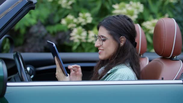妇女坐在可转换汽车上浏览平板电脑 女司机用小玩意在出租车上看着摄像头 — 图库视频影像