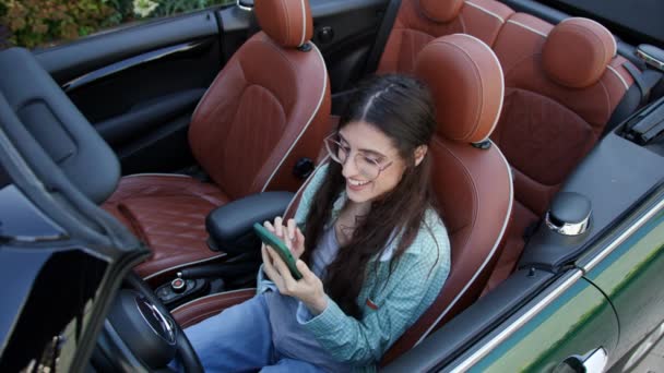 坐在可换车内的妇女在电话上阅读好消息 女司机很喜欢用智能手机开车 — 图库视频影像