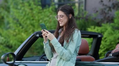 Üstü açık arabada cep telefonuyla mesajlaşan kadın. Sürücü arabanın yanındaki akıllı telefonu tarıyor. 4K