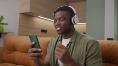 Kulaklıklı Adam Şarkı Söylüyor Cep Telefonu Tutuyor. 20 'li yaşlarda erkek, evdeki kanepede oturan akıllı telefonu kullanarak müzik dinlemekten hoşlanır. 4K