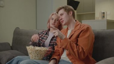 20 'li yaşlarda TV izleyen patlamış mısır yiyen bir çift. Erkek arkadaş ve kız arkadaş evdeki kanepede oturarak eğleniyorlar. 4K