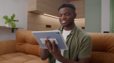 Afro-Amerikalı Adam Tablet Bilgisayarı Koltukta Tarıyor. Siyah erkek dijital tablet kullanıyor. 4K