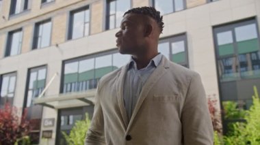 Çapraz kollu bir iş adamı. Dışarıda duran kameraya gülümsüyor. Takım elbiseli Afro-Amerikan bir adam iş merkezinde duruyor. 4K