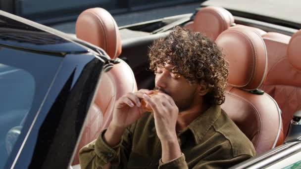 司机吃汉堡看着坐在车里的相机 饥饿的人在可换的地方吃芝士汉堡 — 图库视频影像