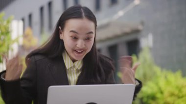 Asyalı Kadın laptopunda iyi haberleri okurken çok heyecanlı. Neşeli iş kadını harika bir iş teklifi alıyor. Kadın çevrimiçi kazanıyor. 4K