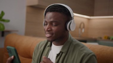 Kulaklıklı Adam Şarkı Söylüyor Cep Telefonu Tutuyor. 20 'li yaşlarda erkek, evdeki kanepede oturan akıllı telefonu kullanarak müzik dinlemekten hoşlanır. 4K