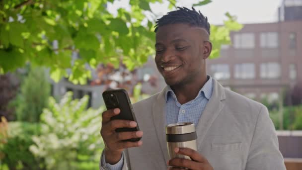 Black Man Sms Mobiele Telefoon Drinkt Koffie Buiten Lachend Vol — Stockvideo
