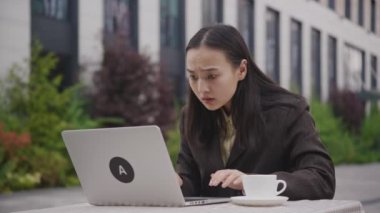 Dizüstü bilgisayarda kötü haber okuyan Asyalı kadın. Dışarıda dizüstü bilgisayar kullanan üzgün bir iş kadını. 4K