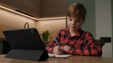 Çalışkan öğrenci bir kalemle yazıyor, online ödevlerine dalmış, tabletine bakıyor. Modern çalışma yöntemleri ve teknolojik entegre öğrenme