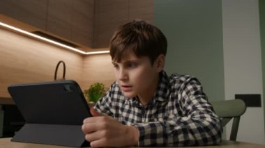 Odaklanmış ve meşgul bir otistik çocuk çevrimiçi öğrenimi bir tabletle kucaklıyor, kendini evdeki konfordan gelen zengin edici bir video dersine sokuyor.