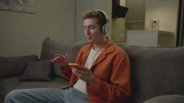 Kablosuz Kulaklıkla Müzik Dinleyen Adam. Genç yetişkinler evdeki koltukta oturan cep telefonlarıyla müzik dinlemeyi severler. 4K