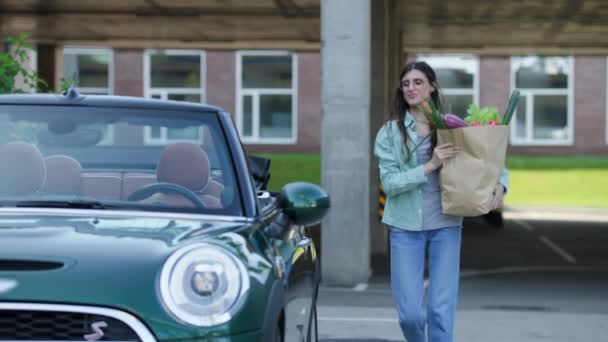 女人把购物袋放进可换车内 年轻的成年女性提着装有新鲜食物的袋子上车 — 图库视频影像