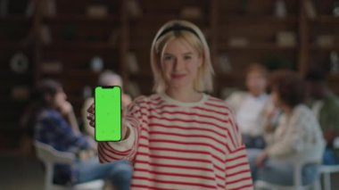 Kendine güvenen genç bir kadın bir terapi grubunun önünde elinde dijital sunum için yeşil ekranlı bir akıllı telefon tutuyor.