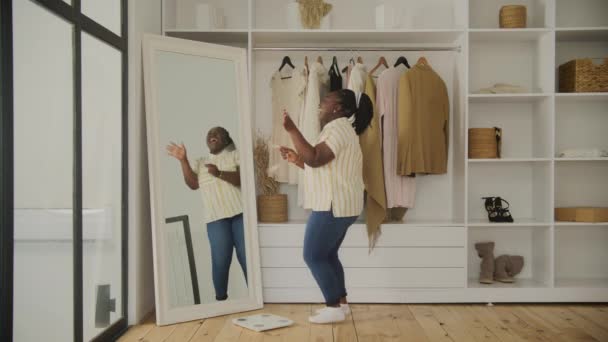 一个快乐的女人在一个宽敞的小房间的镜子里欣赏着自己的倒影和减肥的进步 — 图库视频影像