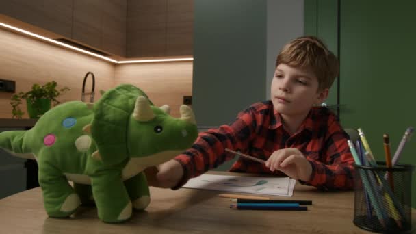 Сфокусированный Ребенок Наслаждается Рисованием Кухонным Столом Красочной Плюшевой Игрушкой Динозавра — стоковое видео