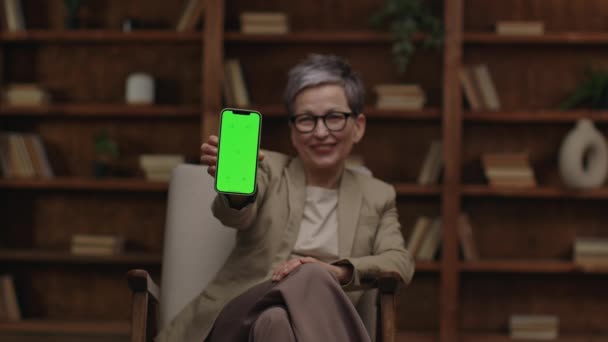 快乐的治疗师用绿色屏幕 木制书架背景展示手机 — 图库视频影像
