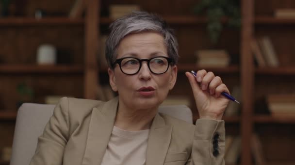 Selbstbewusste Seniorin Mit Brille Spricht Und Gestikuliert Mit Stift — Stockvideo