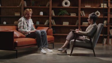 Modern, kitap kaplı ofis ortamında müşterisi olan olgun bir terapist.